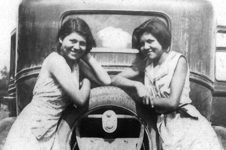 Black and white image of two women leaning on an old car.