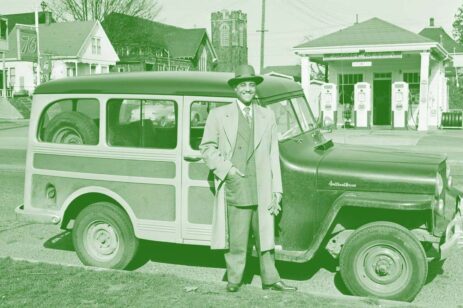 Old image of a man standing in front of his car.