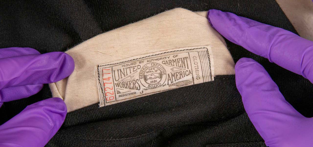 Hands in purple latex gloves, examining a garment label.