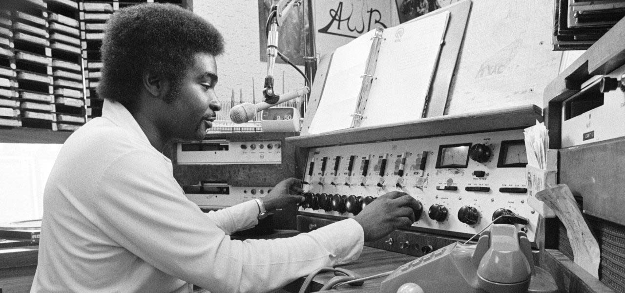 Black and white photo of a man using an old radio station soundboard.