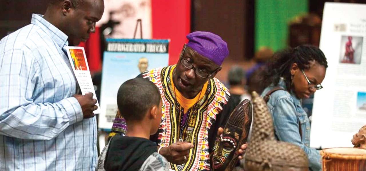 African-American man dressed in traditional African dress, speaking with a young boy.