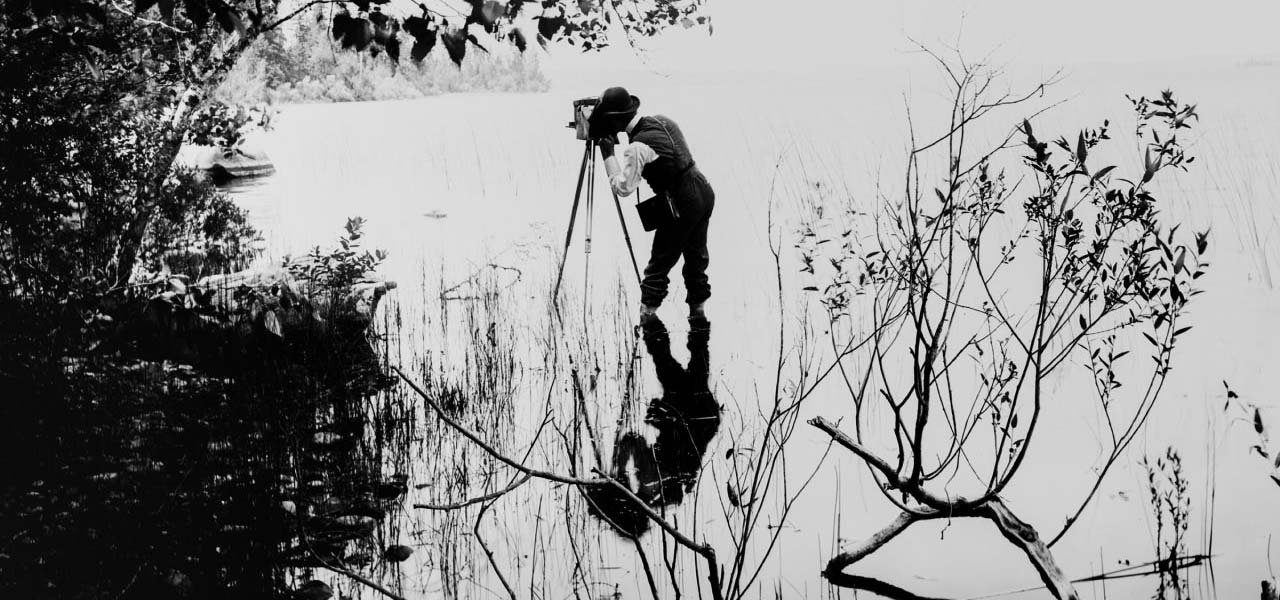 Photo of a man taking a photo while standing in a lake.