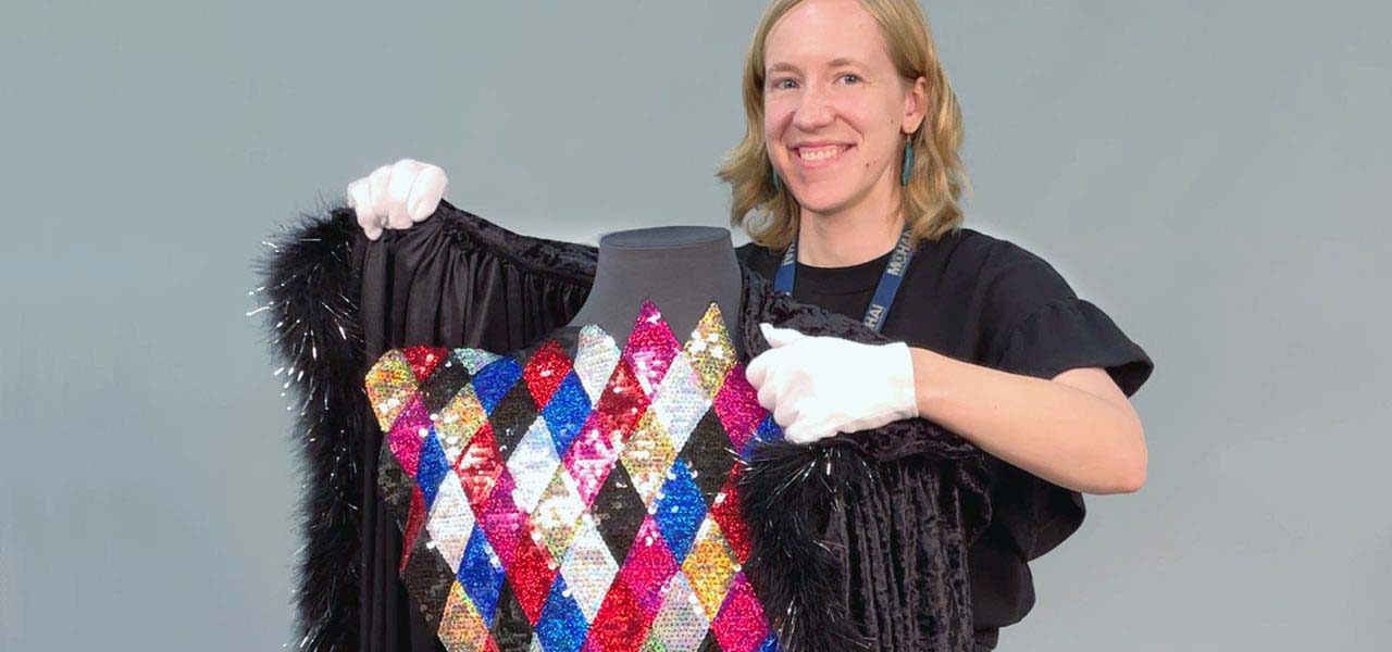 Blonde, smiling woman putting a fury black coat over a colorful sequined dress.