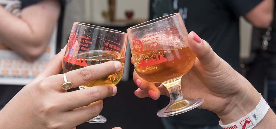 Two hands toasting cider tasting cups together.