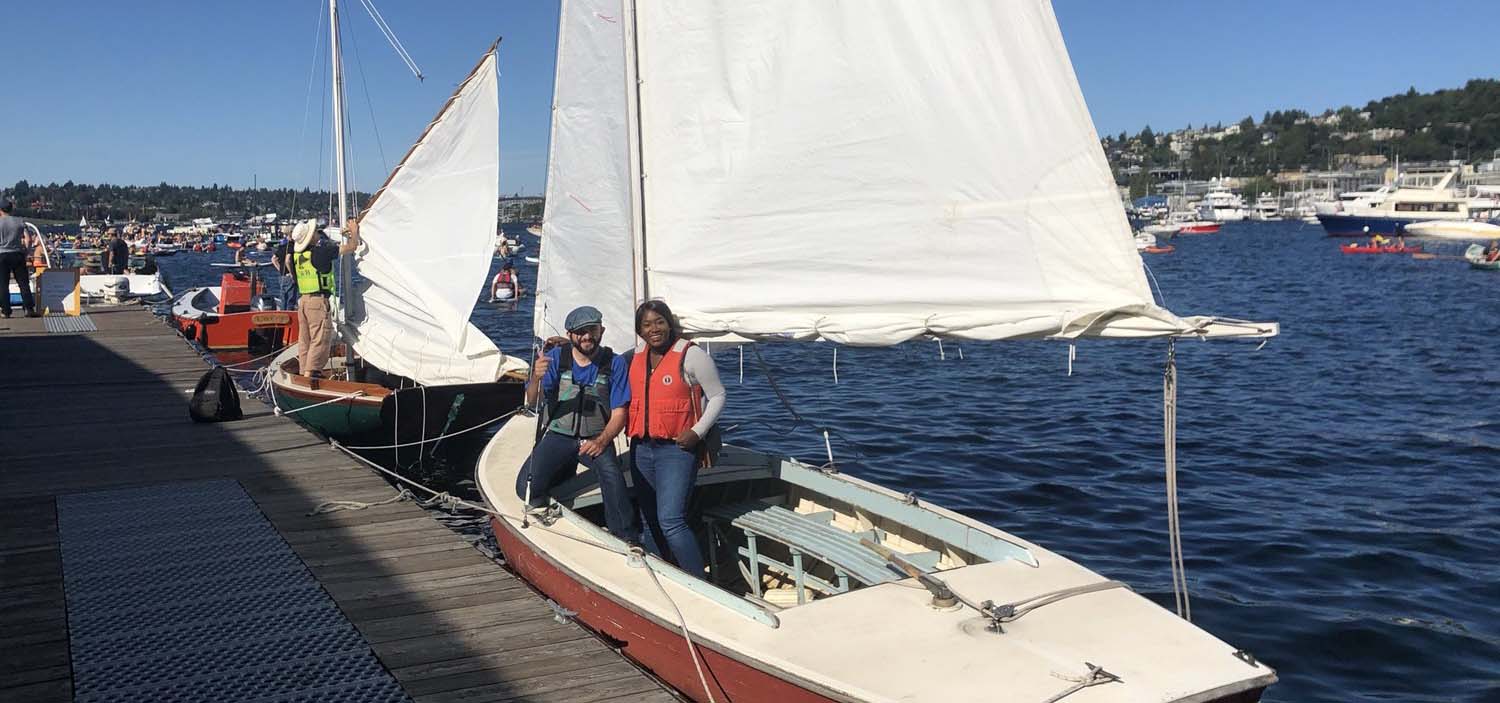 Two people about to sail on a small sailboat.