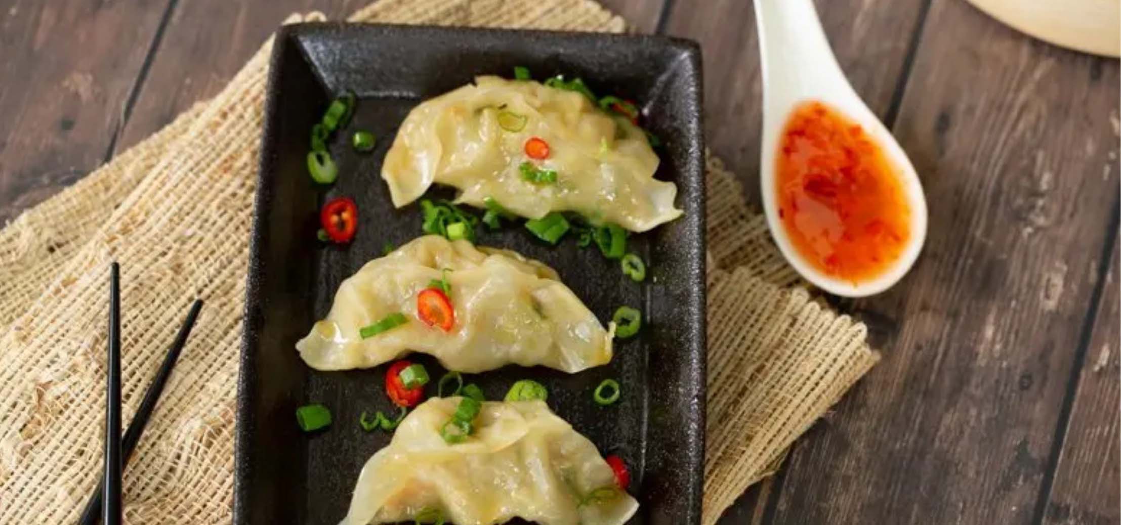 Shrimp dumplings on a small black tray with a side of chile oil.