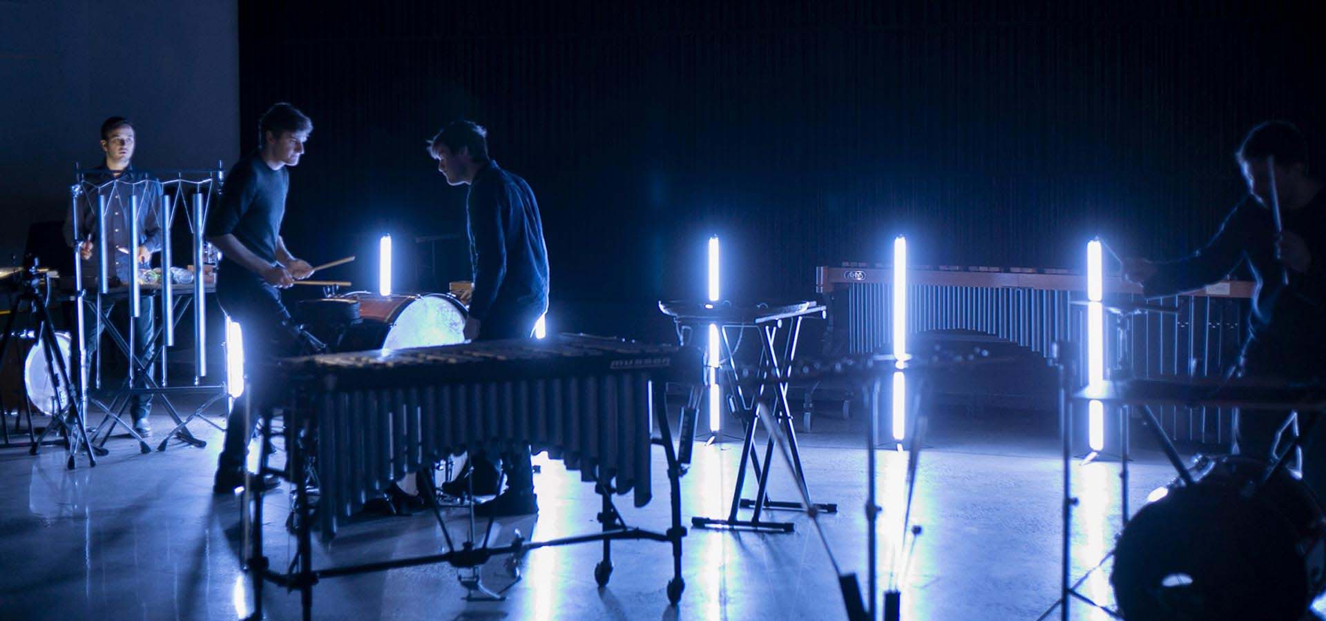 Percussion band playing in the dark with neon lights illuminating the performance.