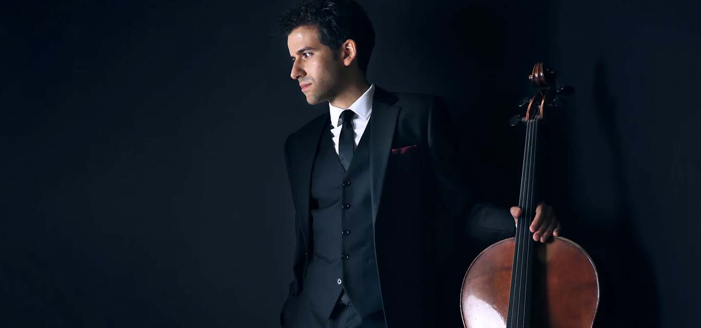 Man in a black suit holding his cello.