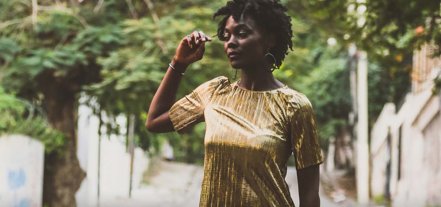 Woman in a gold dress outside by trees, playing with her hair.