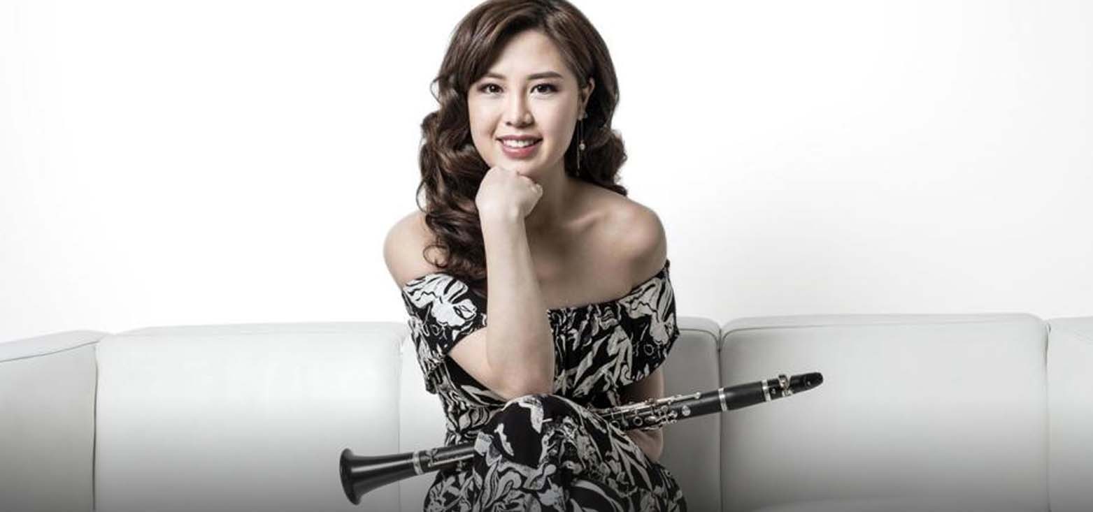 Woman holding her clarinet posing on a couch.