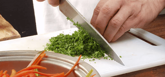 Close up of a man finely chopping herbs.