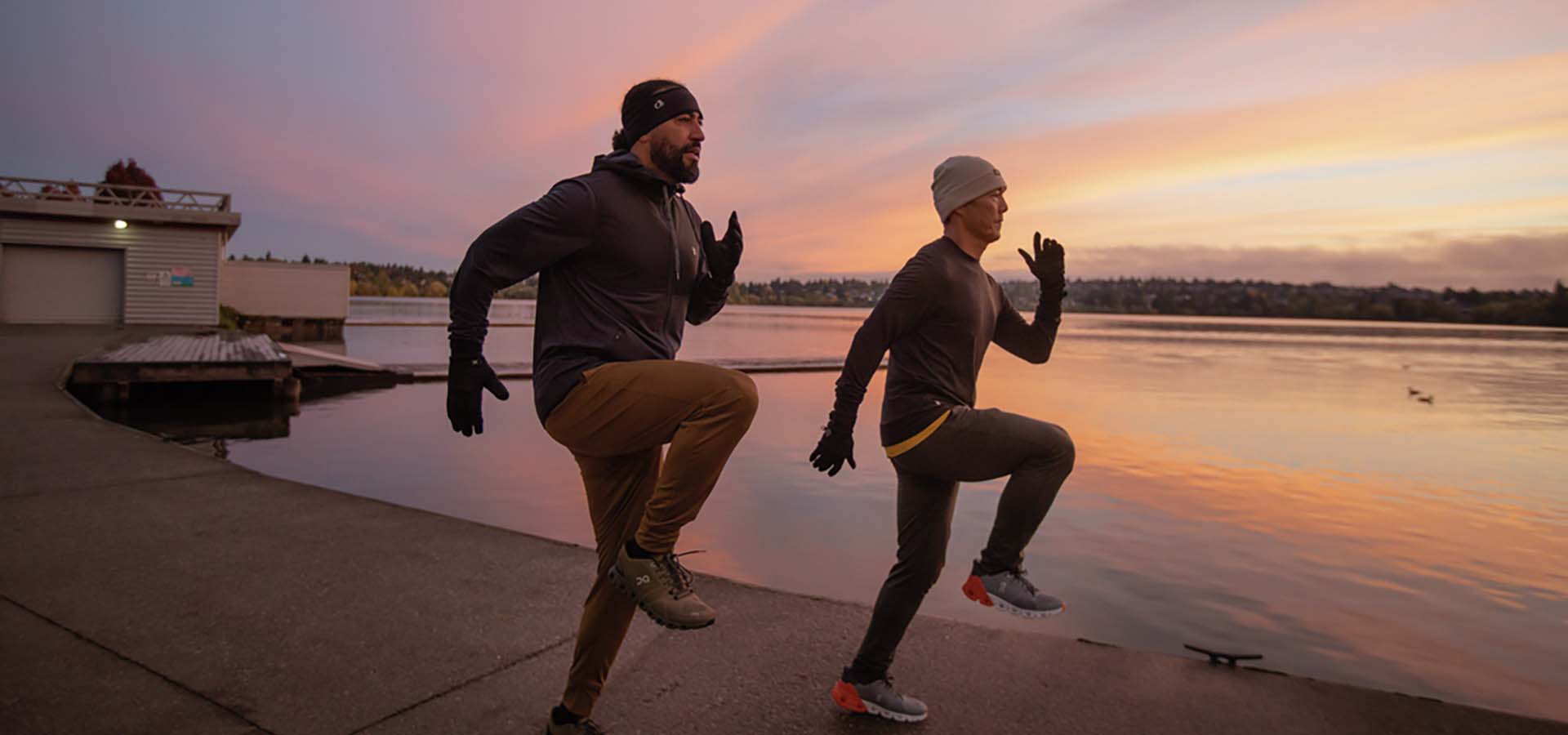 Two men jogging near a lake at sunset.