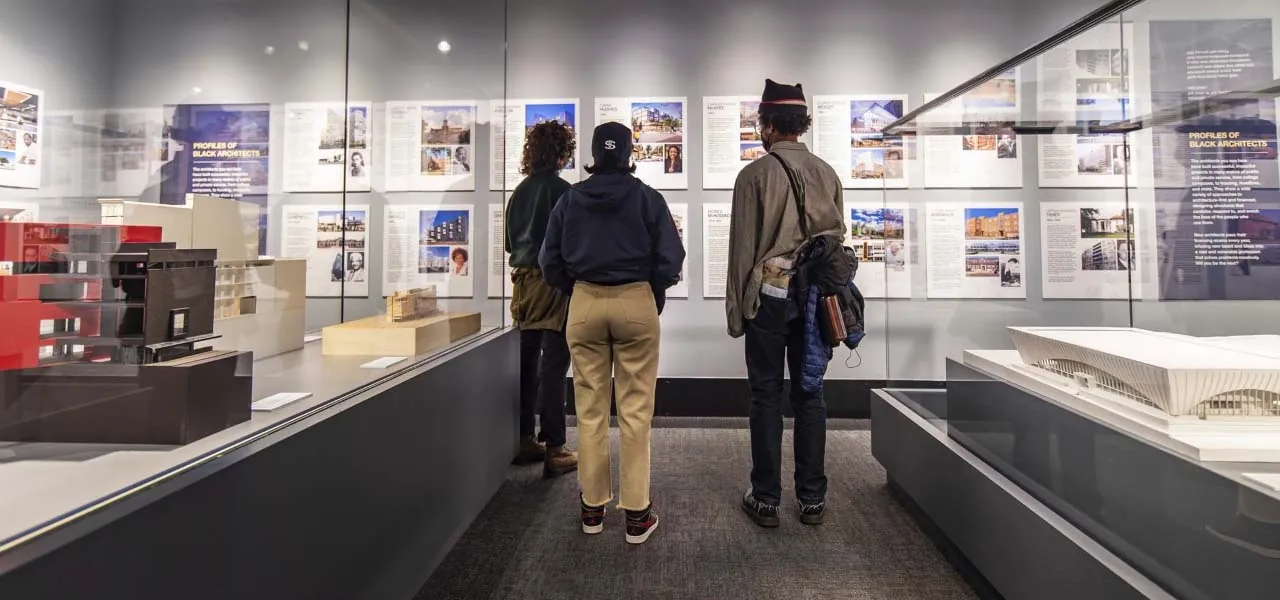 Three people looking at a museum exhibit wall.