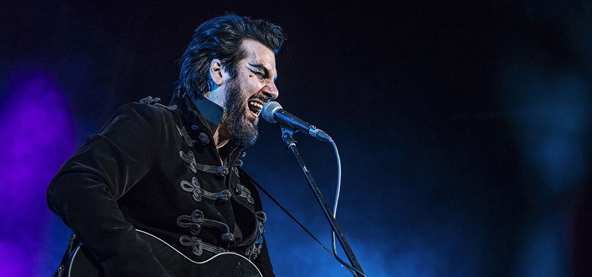 Man singing into a microphone and playing a guitar.