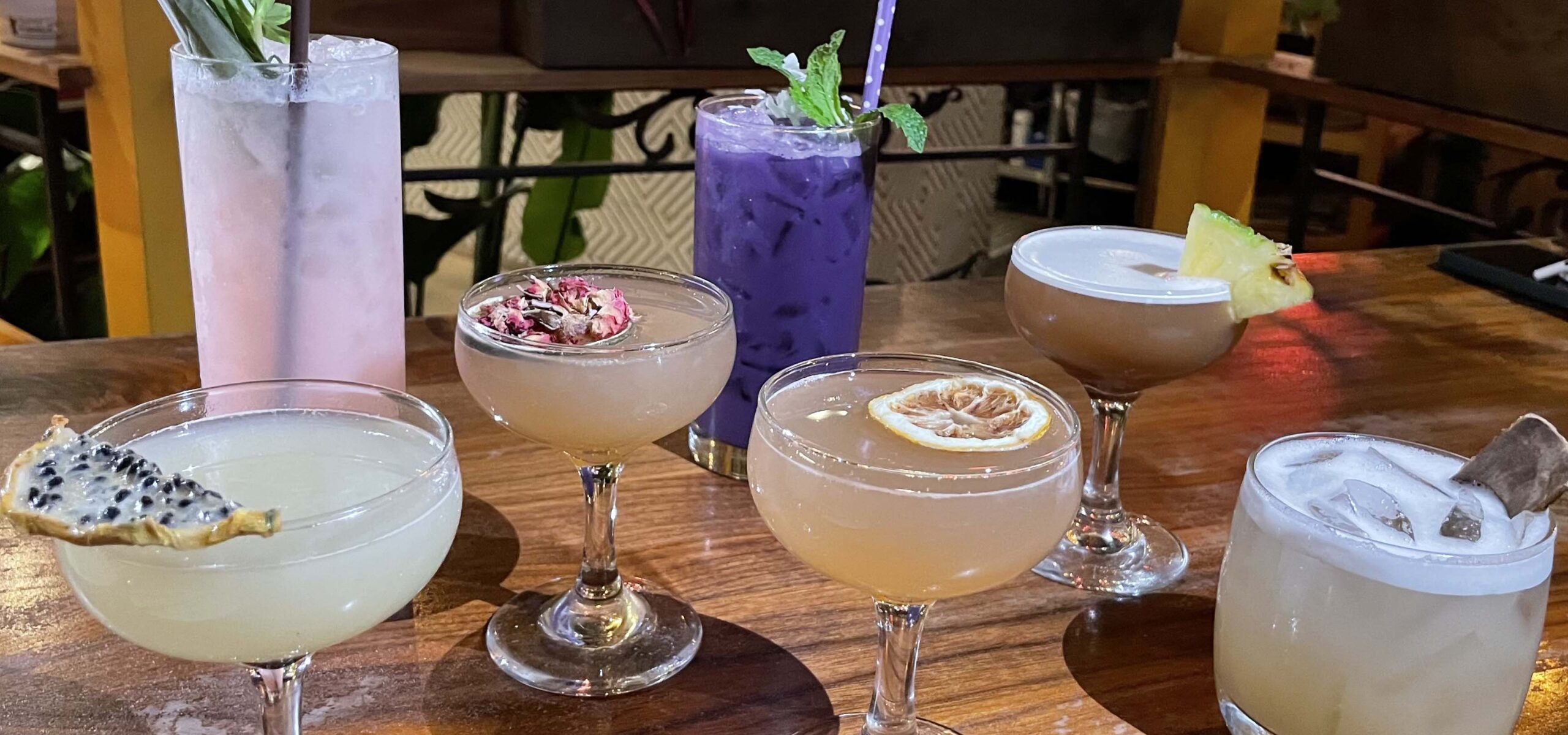 Row of brightly colored beverages on a woodtop bar.