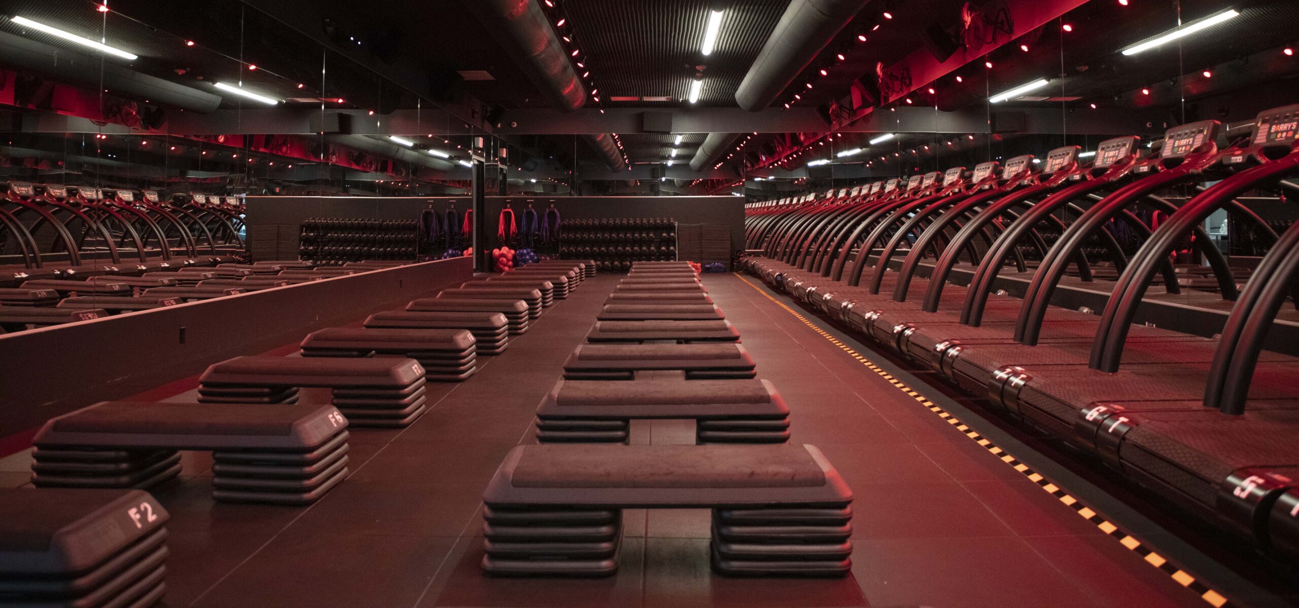 Interior photograph of a gym with rows of treadmills illuminated with red light.
