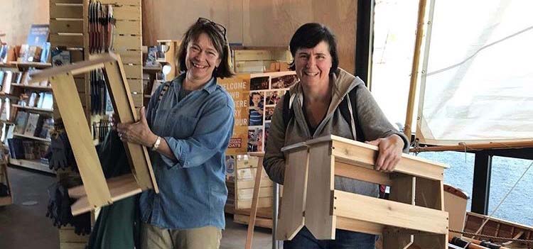 Two women holding up wooden stools they just built.
