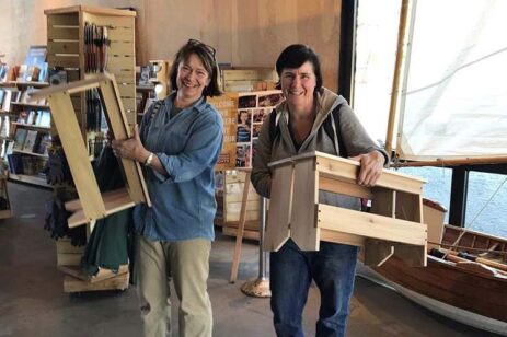 Two women holding up wooden stools they just built.