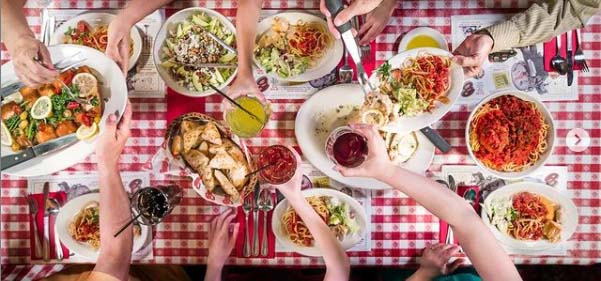 Bird's eye view of a table filled with Italian family-style dishes and people reaching for them.