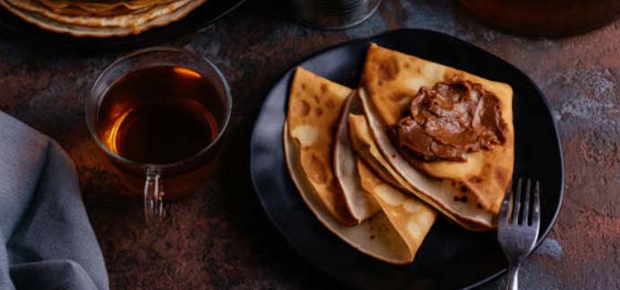 A plate of crepes with chocolate sauce and a cup of tea on the side.