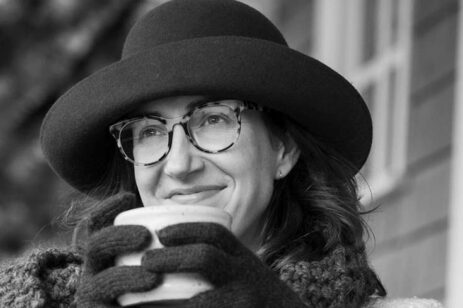 Black and white photograph of a women wearing a hat and sipping a cup of soup.