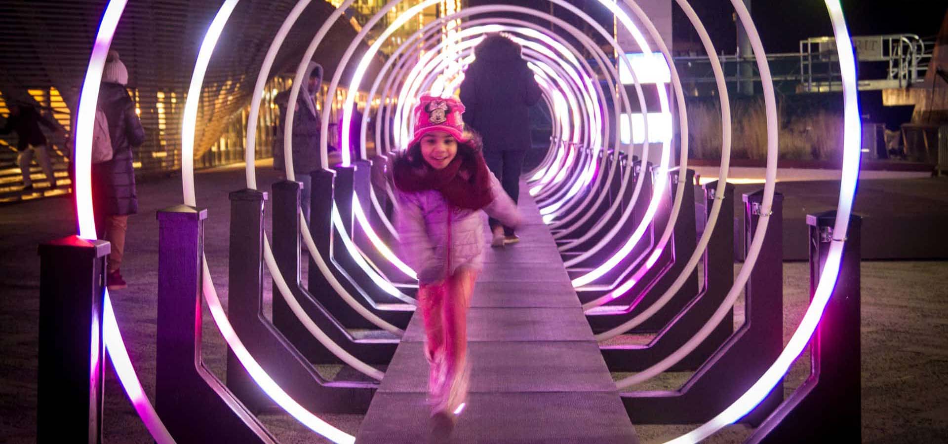 Girl walking through a neon tube outdoor art installation.