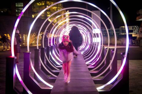 Girl walking through a neon tube outdoor art installation.