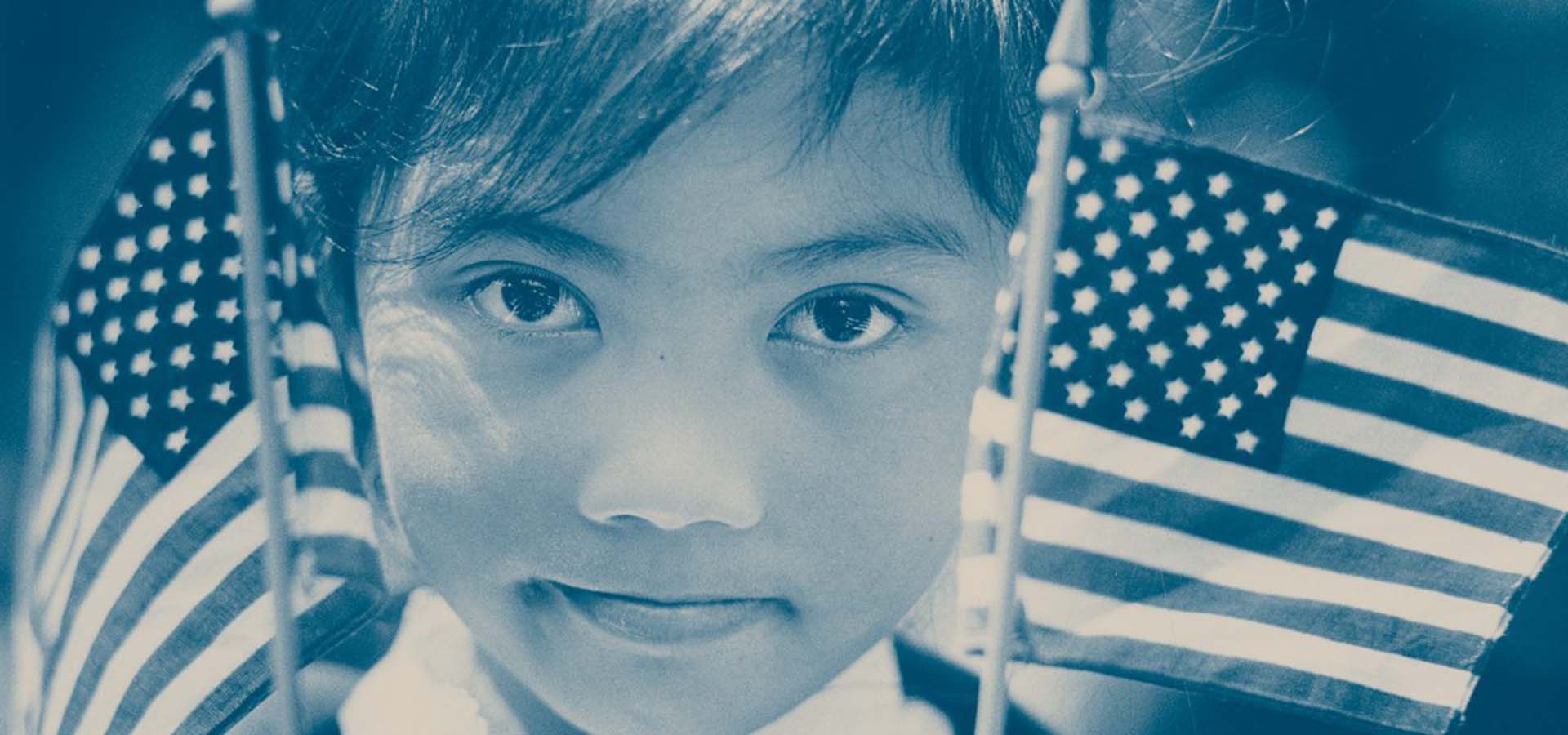 Blue tone photography of a minority child holding American flags.