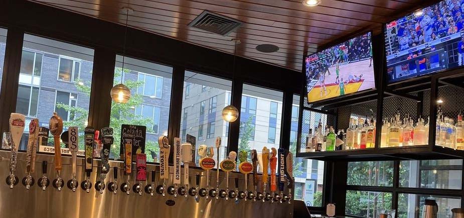 A row of taps below a couple TVs broadcasting sports.