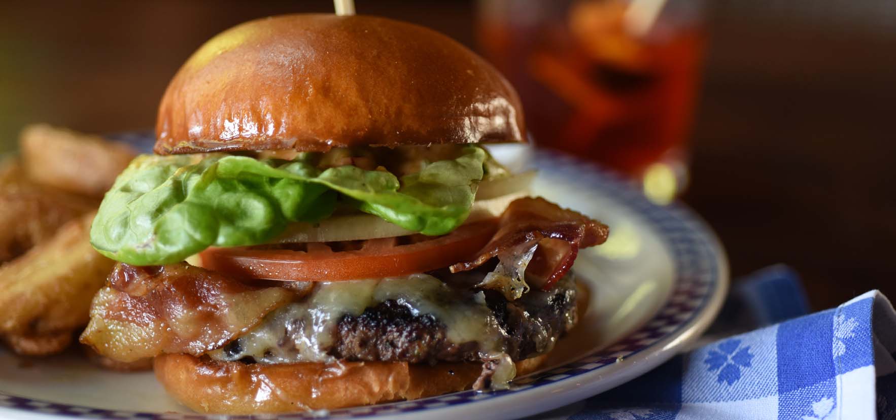 Close up image of a bacon cheeseburger with a side of steak fries.