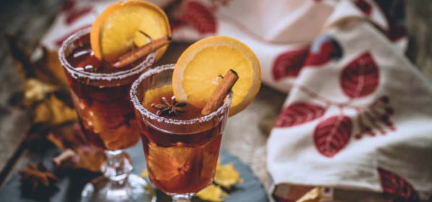 Two fall cocktails topped with orange slices and cinnamon sticks.
