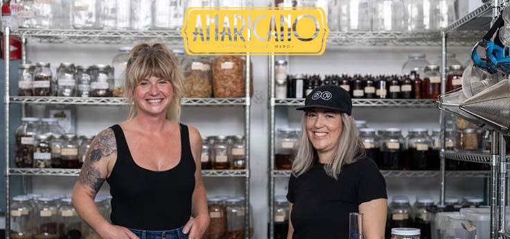 Two women in an industrial kitchen setting up for a cocktail class.