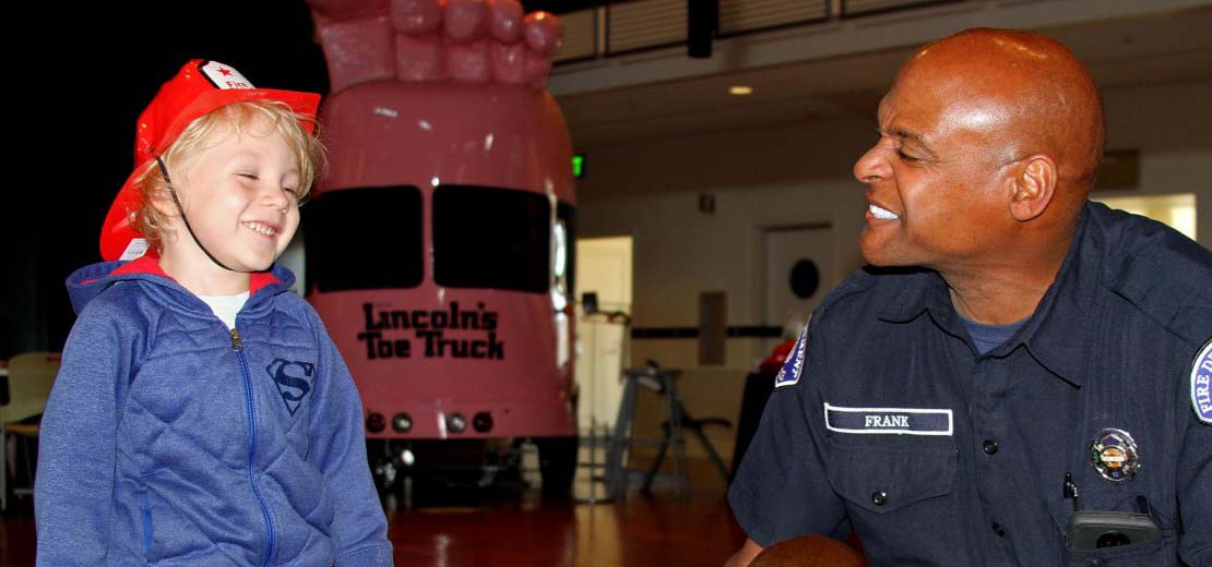 Fireman smiling at a boy in a fireman's hat.