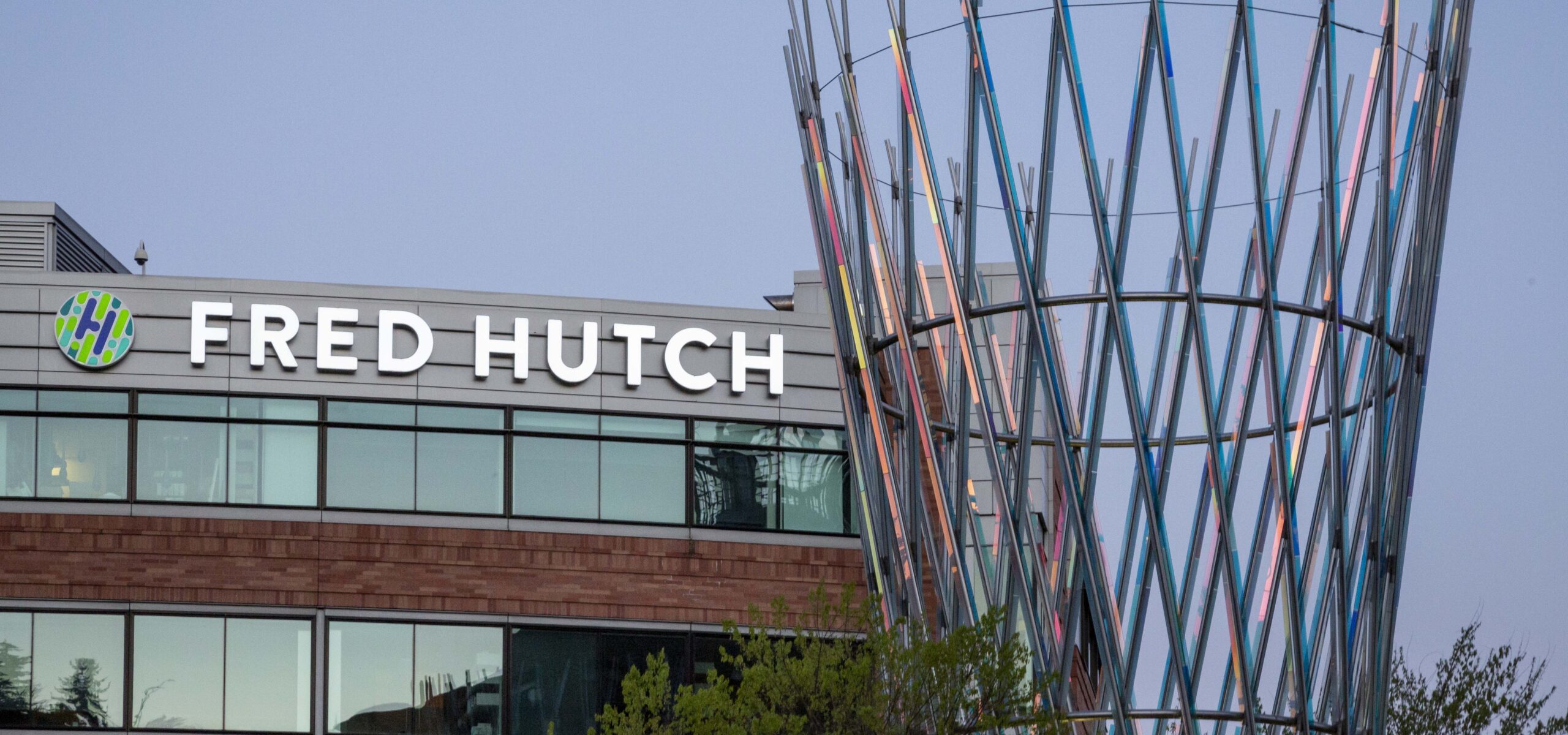 View of the neon marquee sign of the Fred Hutch campus with some woven metal outdoor art sculpture in the foreground.