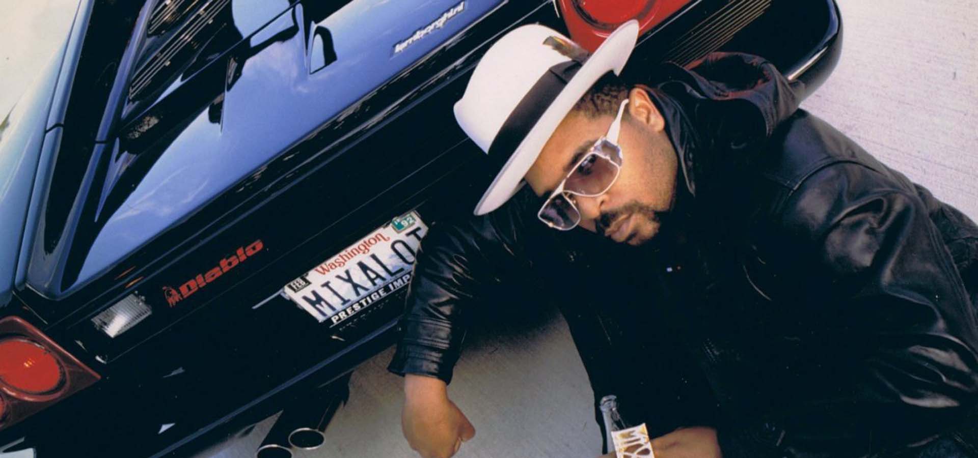 Rapper Sir Mix-A-Lot kneeling by a black sports car.