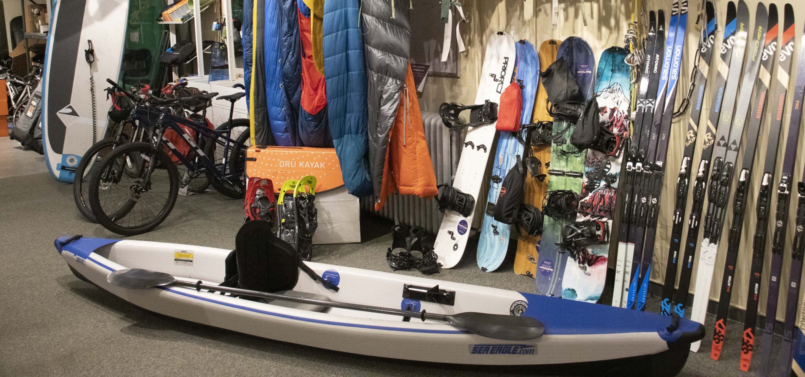 Wall arranged full of outdoor adventure gear like skis, sleeping bags, kayaks, etc.