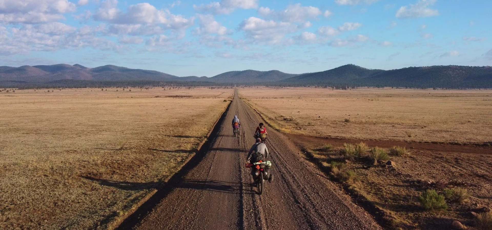 Three people riding bikes on a dirt road.