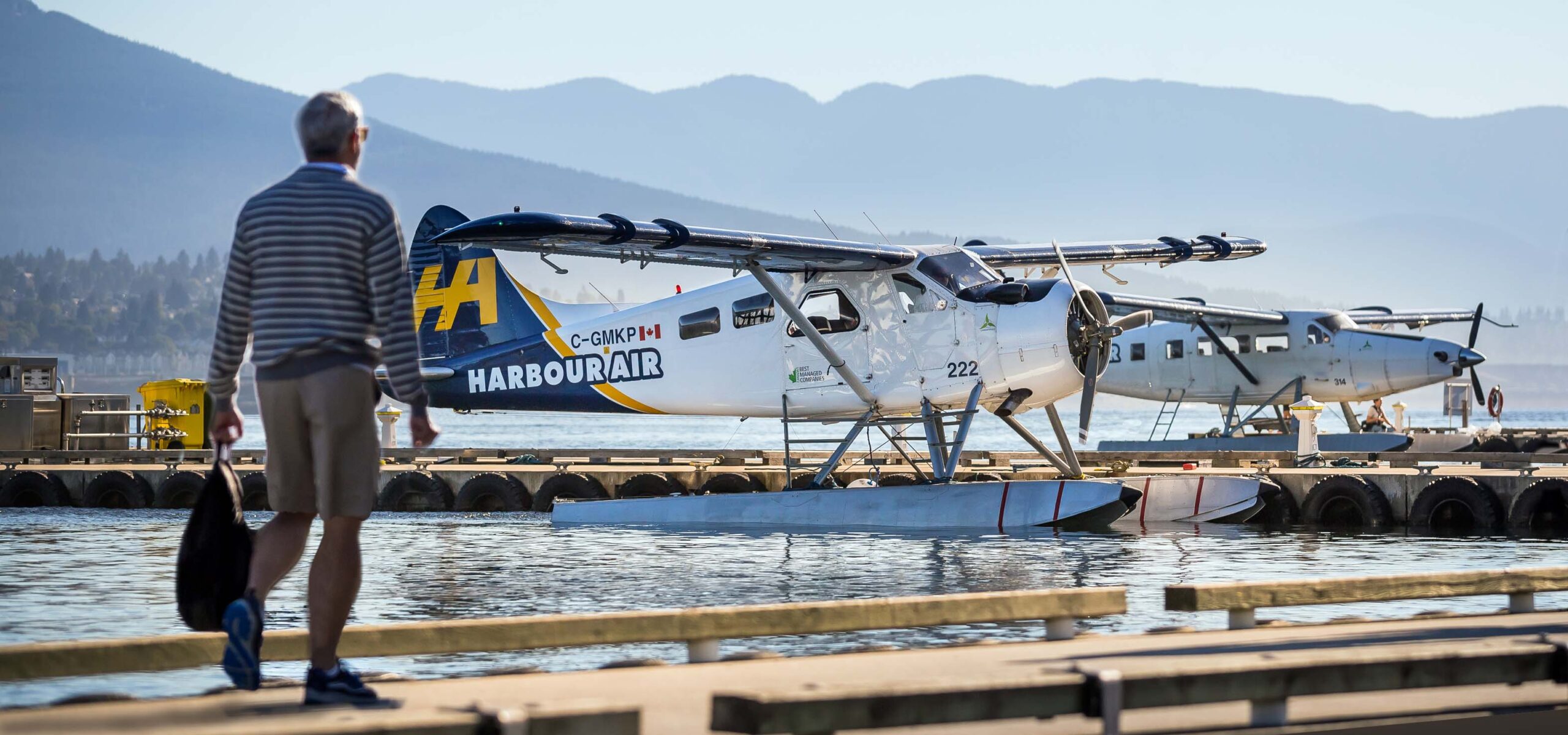 Man walking on a pier to board a seaplane moored on a lake.