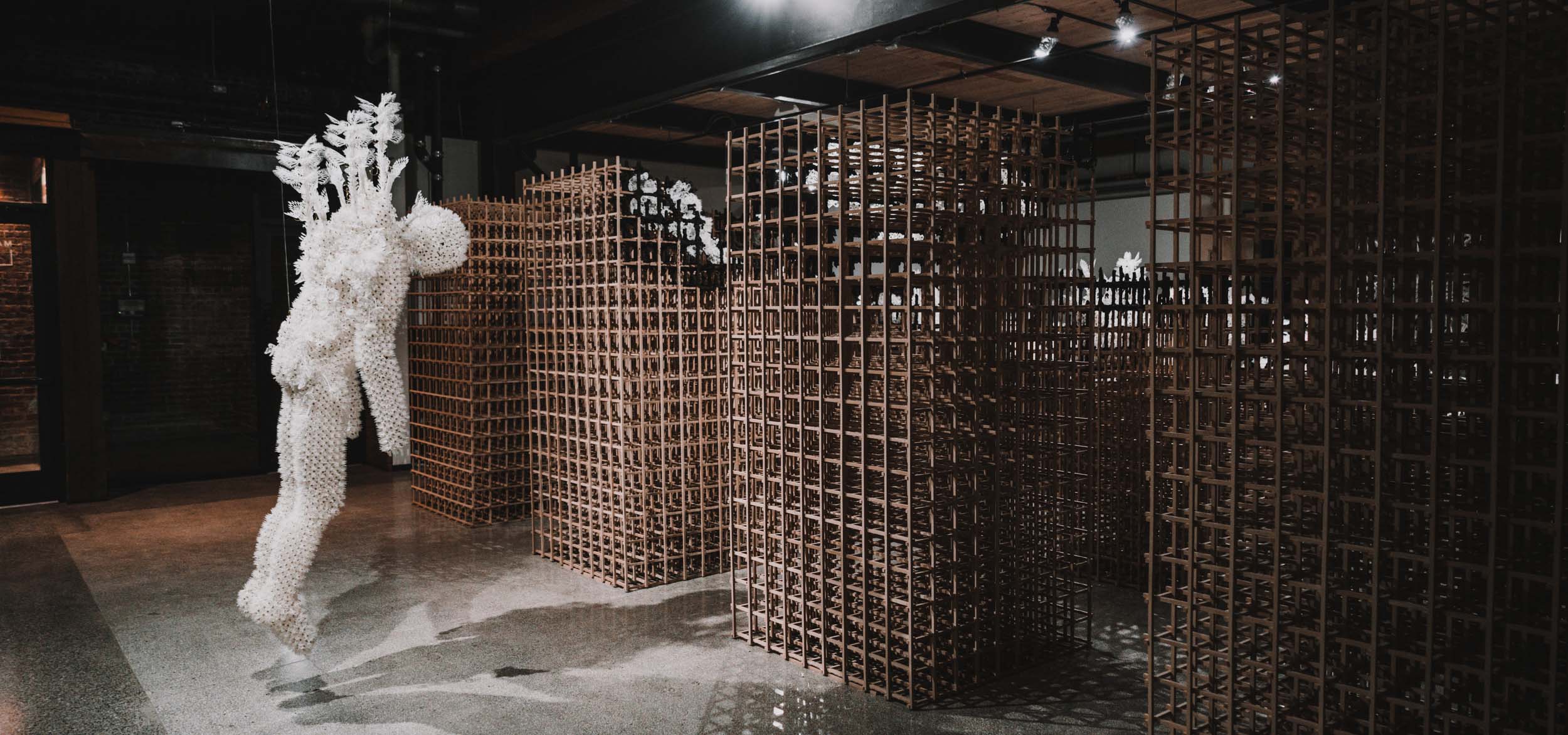 Seattle-based kinetic sculptor Casey Curran's hanging figure made of paper hanging in front of labyrinth-like wooden towers.