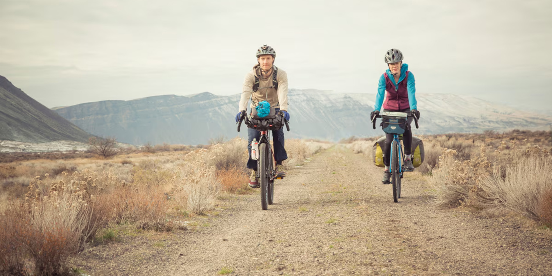 two people cycling on trail in mountains