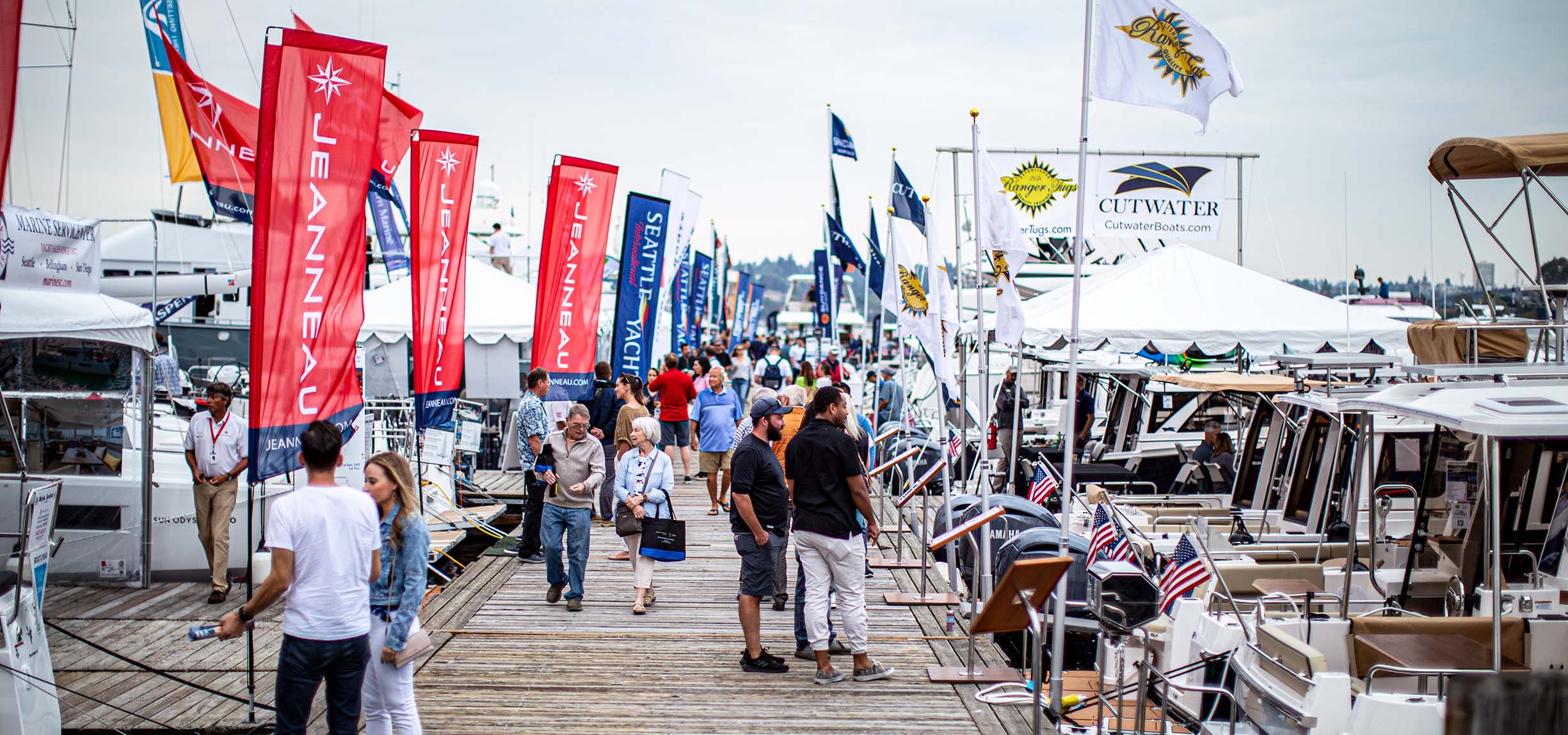 People explore yachts on a pier.