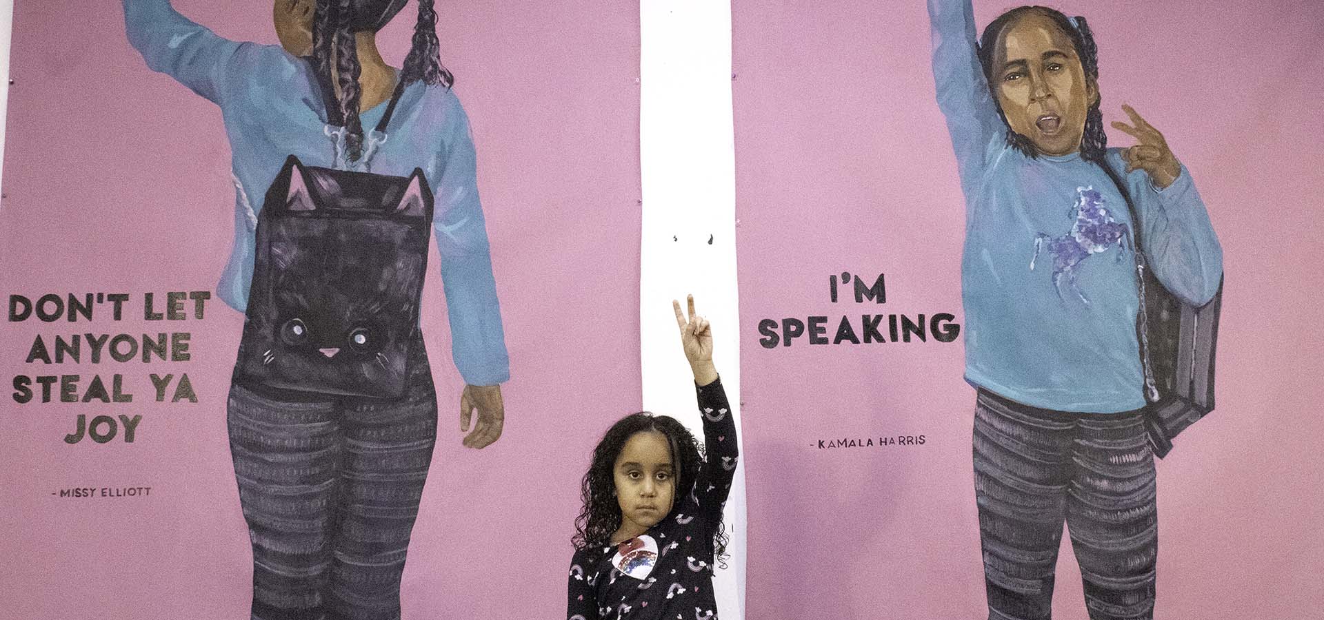 Window mural art featuring an African-American girl with messaging about BIPOC awareness with young girl in front holding up a peace sign with her fingers.