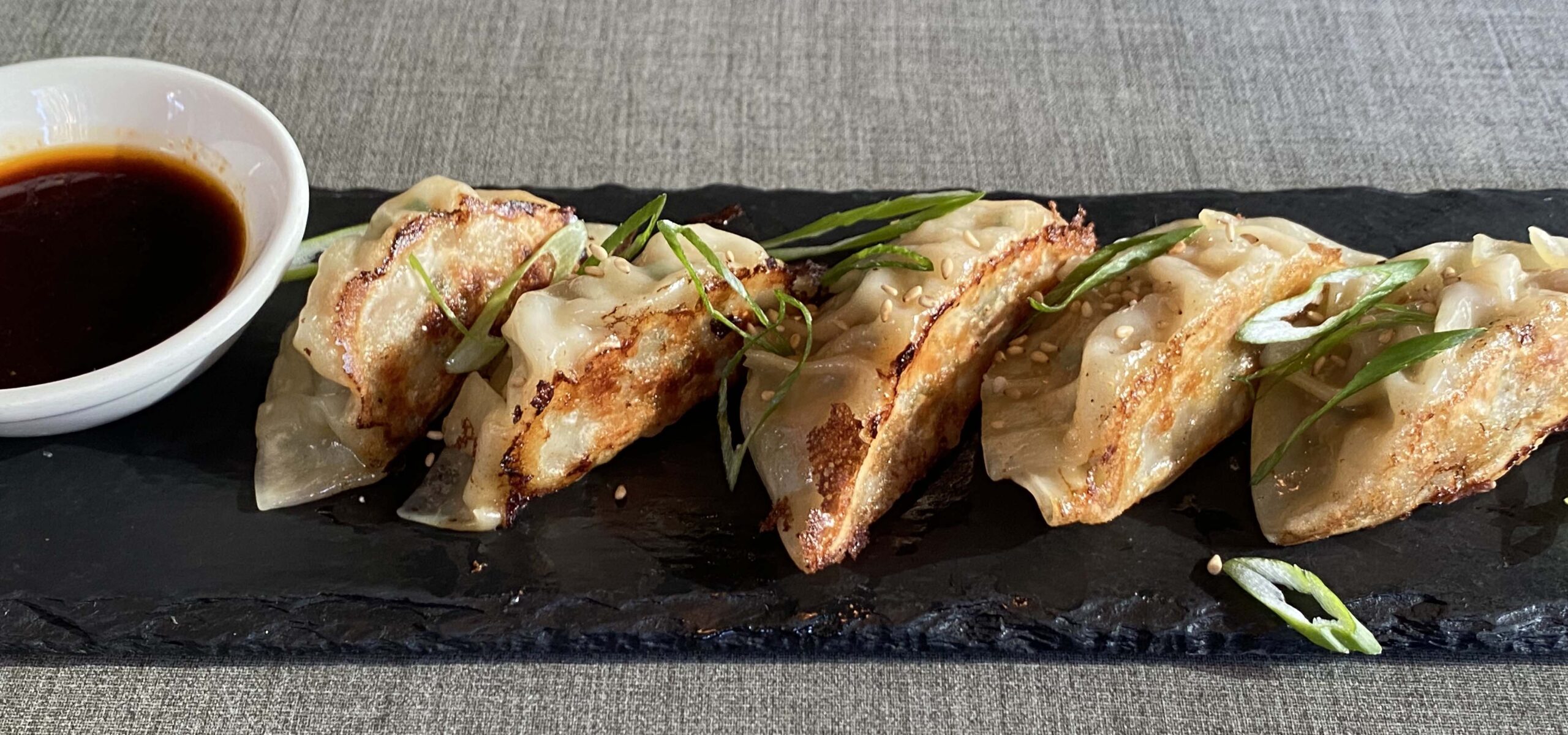 Tray of gyoza or potstickers with dipping sauce on the side.