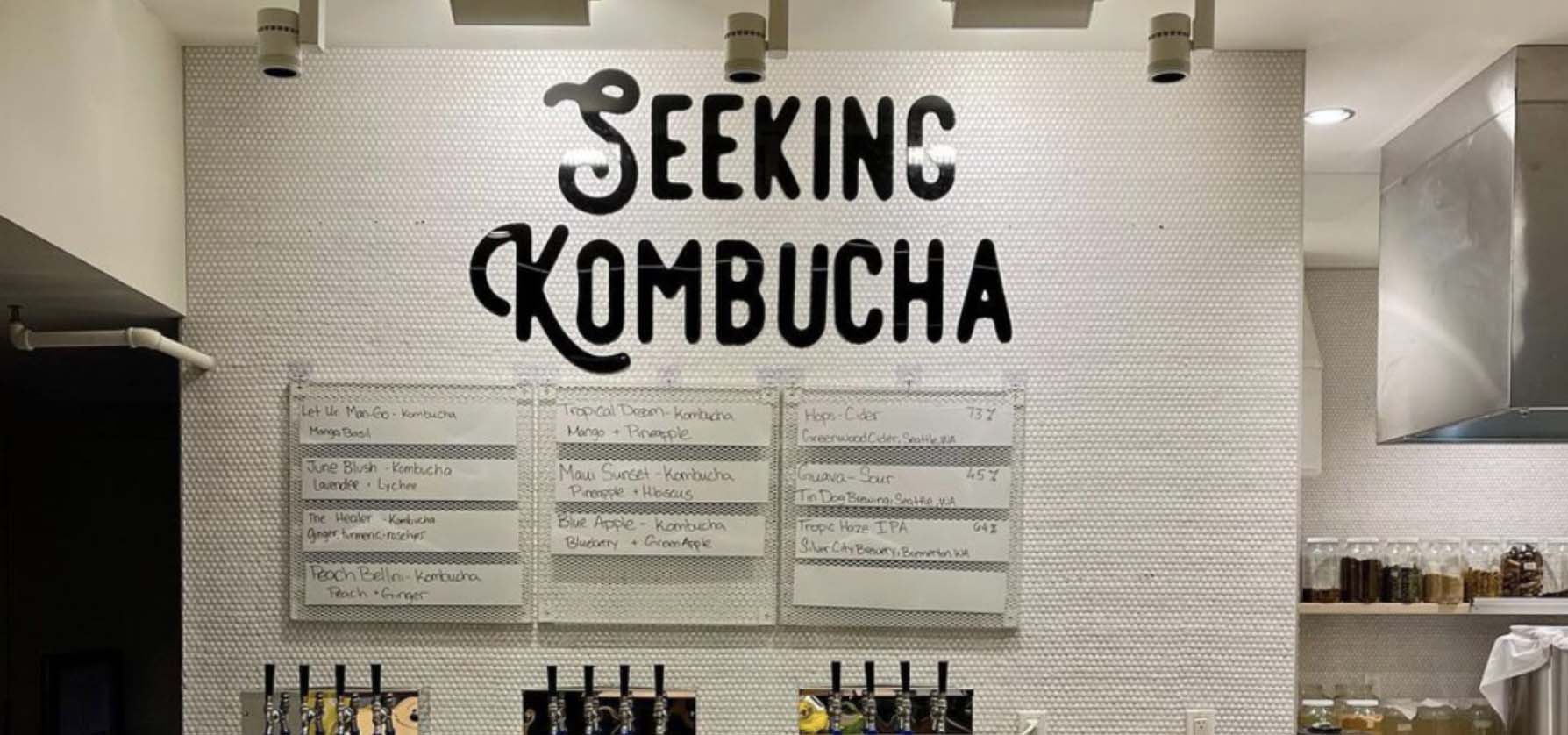 Inside a kombucha shop with menu on the wall and taps on behind the counter.