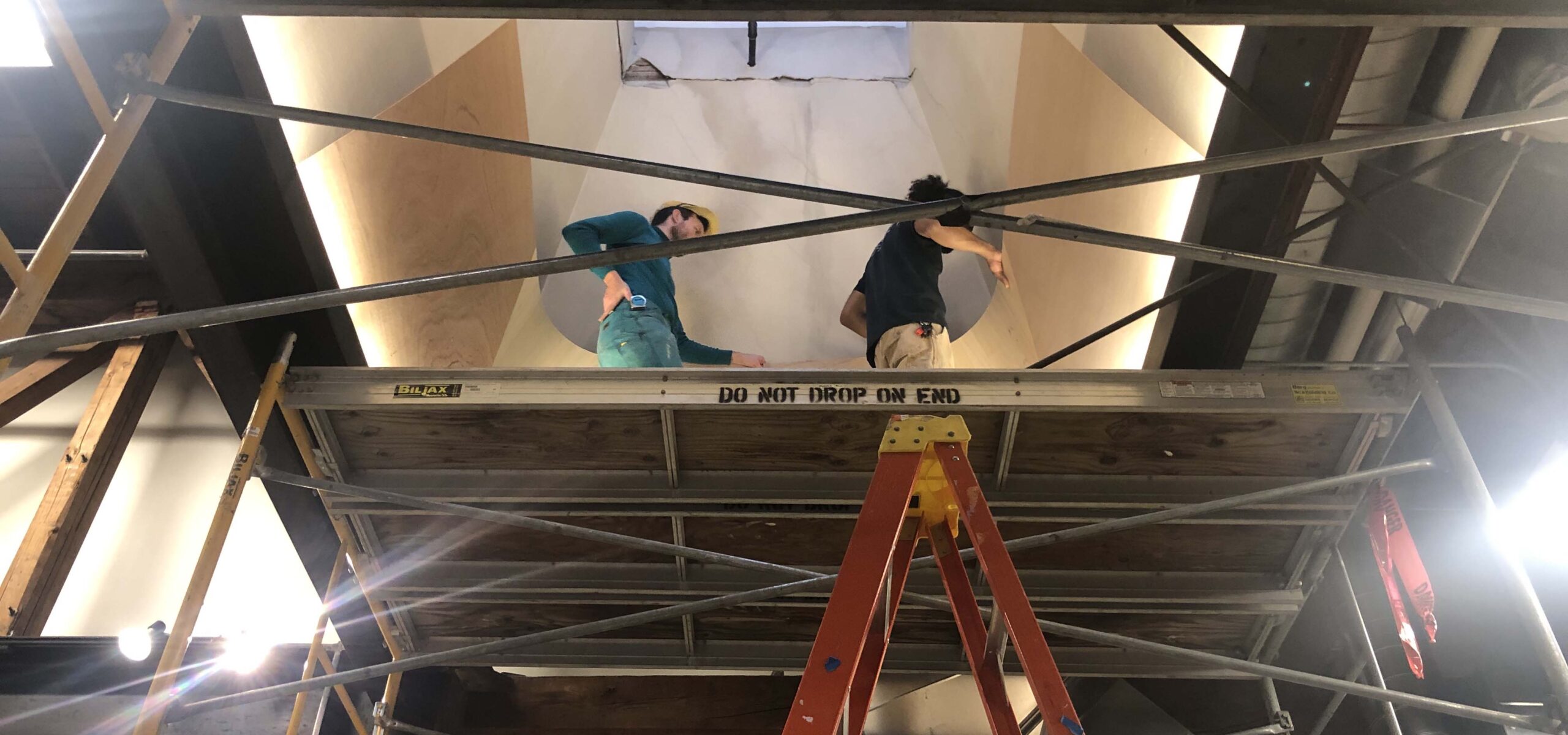 People walking on scaffolding to install a large art display.