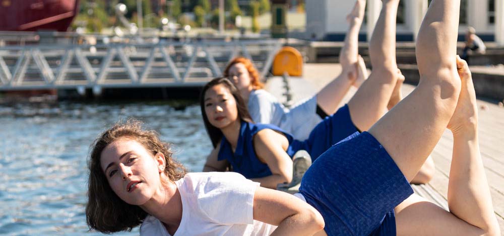 Female dancers perform a dance routine on a lake pier.