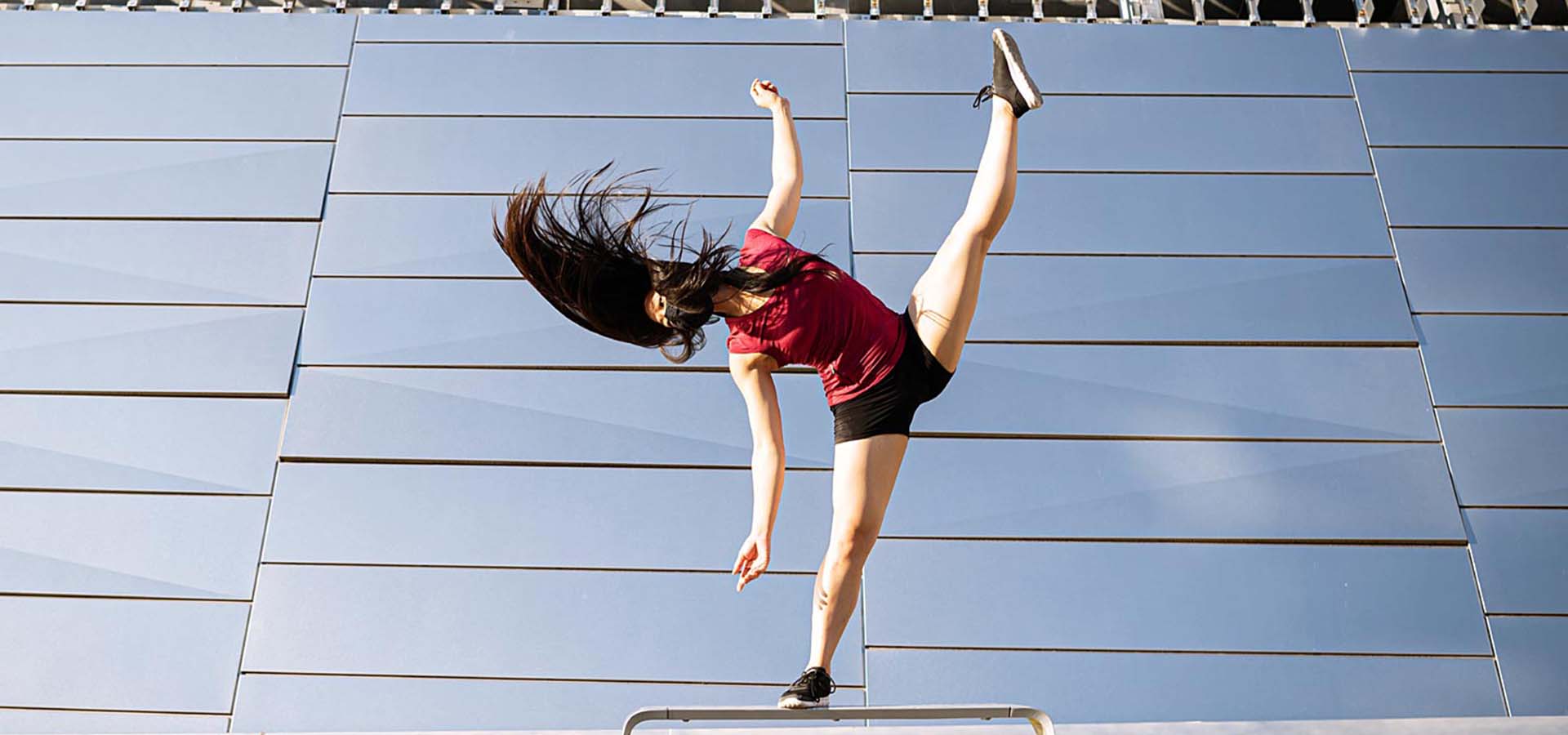 Female dancer balancing on a rail outside a mirrored building.