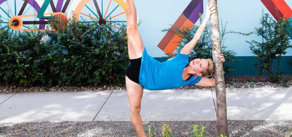 Female dancer performs a split pose near a tree in an urban setting.