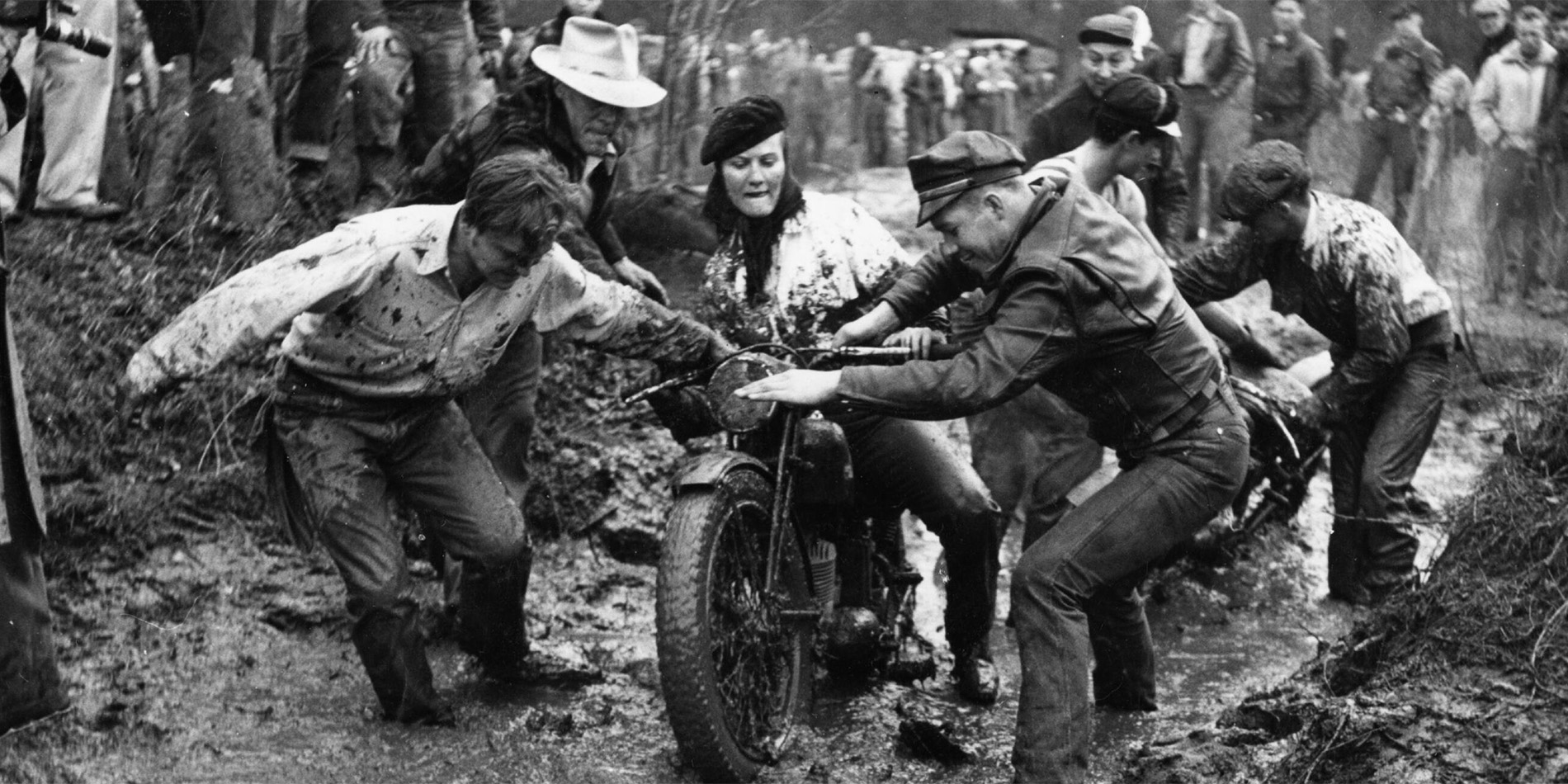historical image of people pulling motorcycle through mud