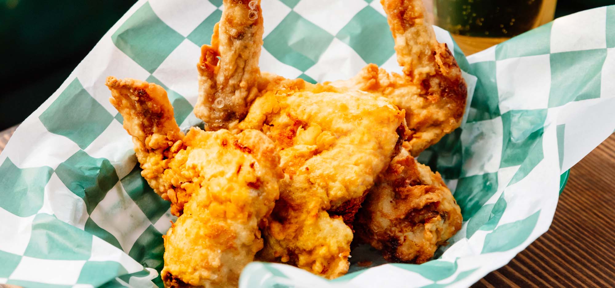 A basket of fried chicken wings on green check parchment paper.
